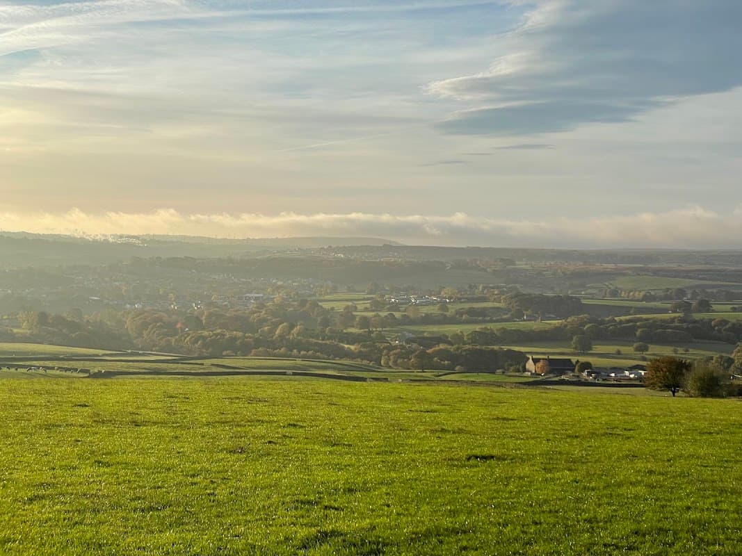 A panoramic view of rolling green hills and valleys under a cloudy sky, with distant villages and trees in the landscape.