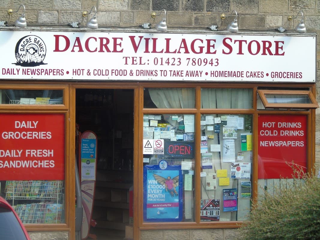 Dacre Village Store storefront with signs for groceries, sandwiches, hot drinks, and an "OPEN" notice.