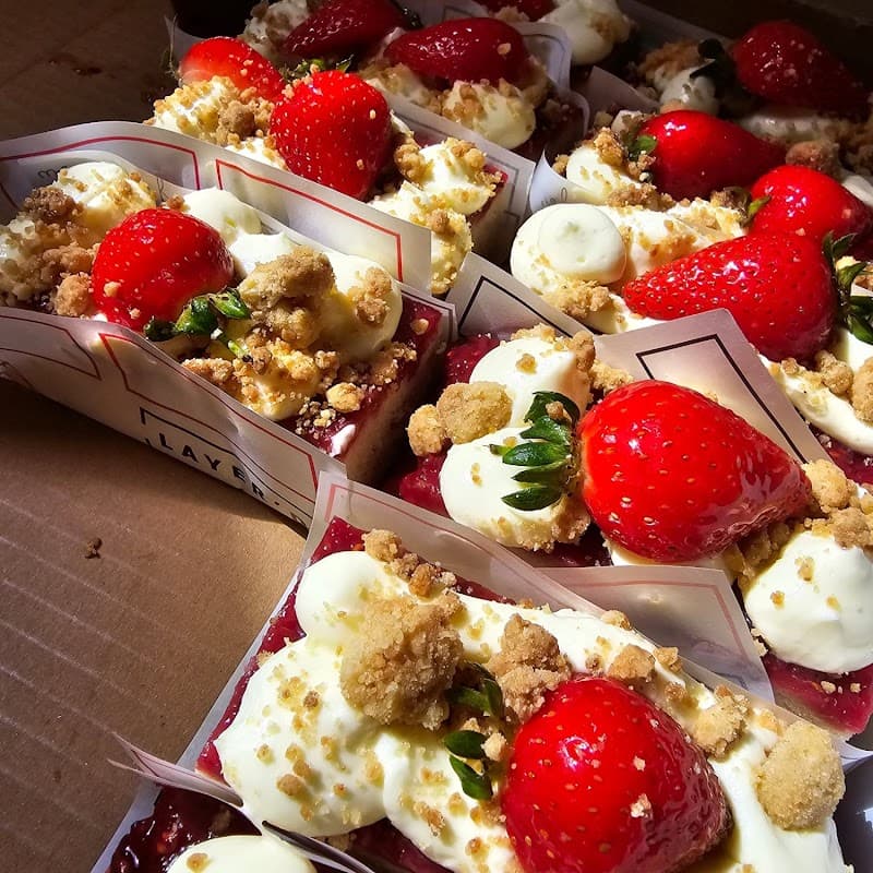 Delicious layered desserts topped with strawberries, cream, and crumbles, arranged neatly in small containers.