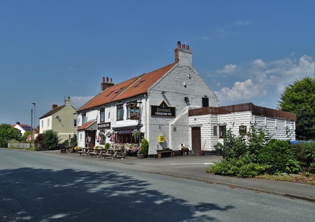 Chequers Inn hotel with a white exterior, red roof, outdoor seating, and lush greenery in Dalton-on-Tees, Yorkshire.