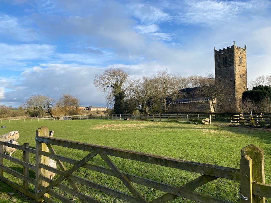 A scenic view of a church tower beside a green field and wooden fence under a blue sky in Danby Wiske, Yorkshire.