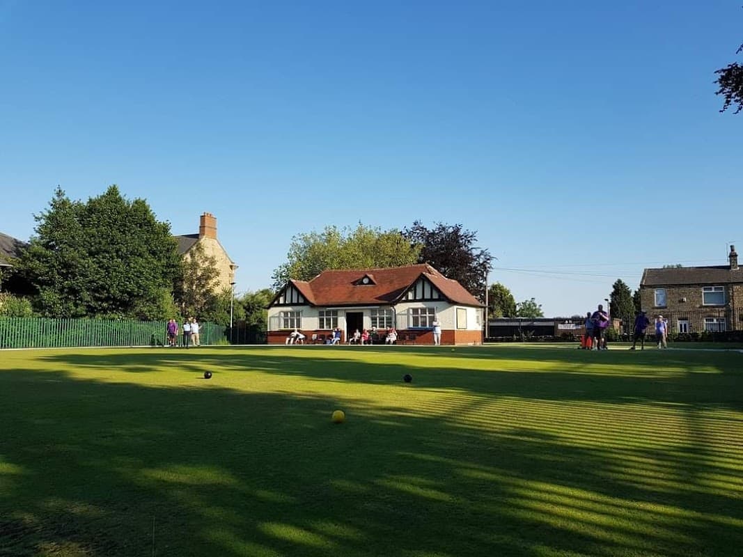 Darfield Park Bowling Club with green lawn, clubhouse, and people playing in the background under a clear blue sky.