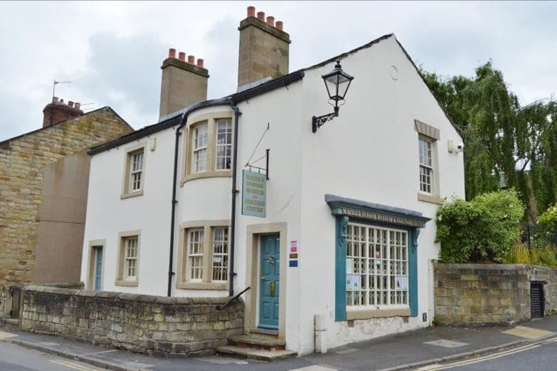 White building with blue door and window shutters, featuring a sign for Maurice Dobson Museum & Heritage Centre.