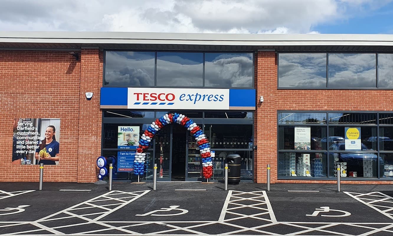 Tesco Express storefront with blue and red balloon arch, signage, and parking spaces in Darfield, Yorkshire.