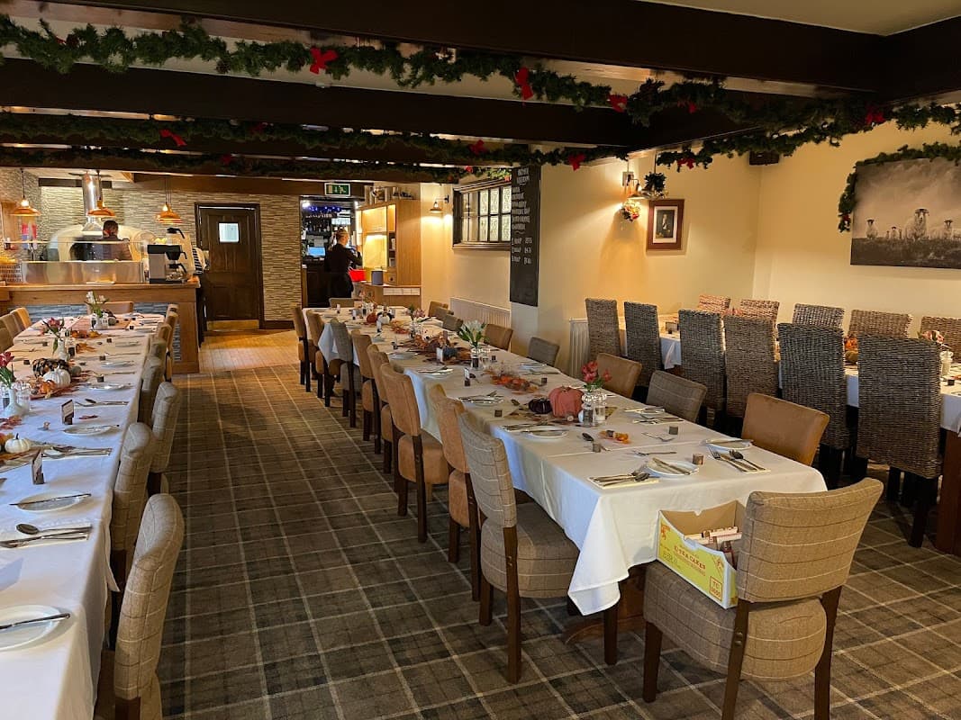 Dining area with neatly set tables, wooden beams, festive decorations, and a view of the kitchen in the background.