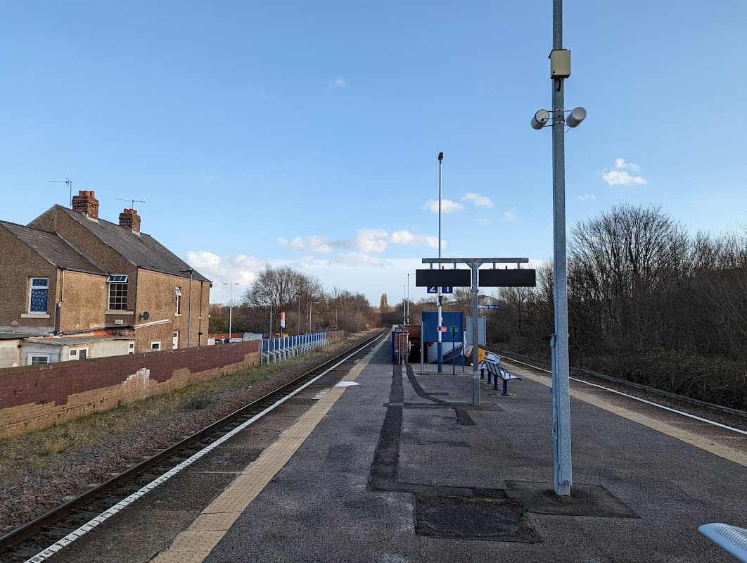 Bus stop at Darnall, Yorkshire, with a platform, benches, and buildings in a rural setting under a blue sky.