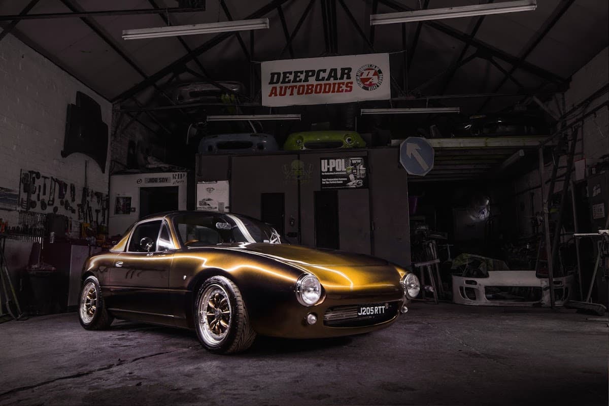A sleek golden sports car with custom wheels inside a workshop, featuring tools and car parts in the background.