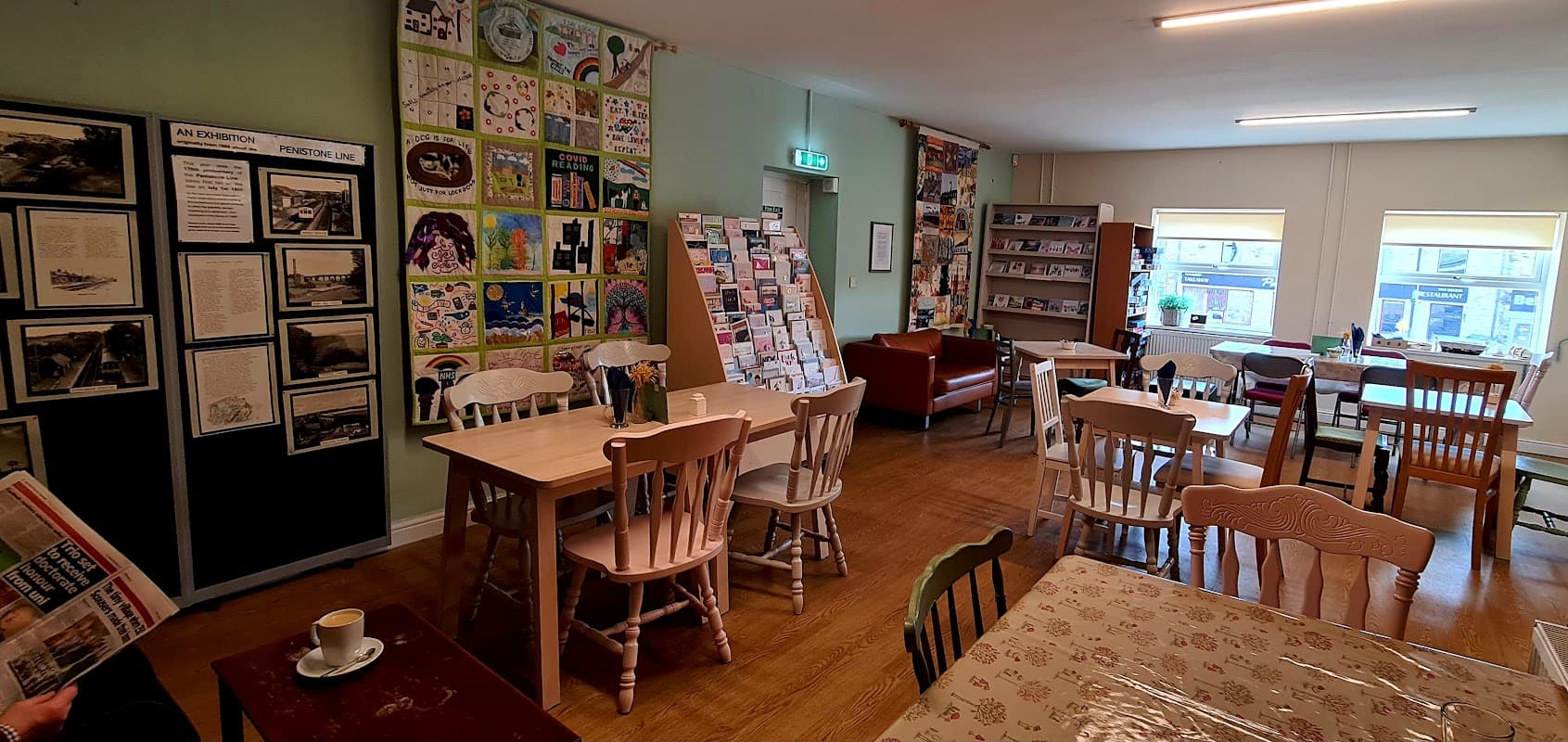 Cozy café interior with tables, chairs, art displays, and bookshelves in Denby Dale Community Library.