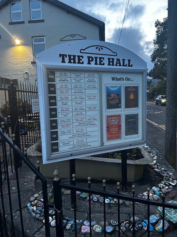 Signboard displaying event schedule and advertisements outside The Pie Hall in Denby Dale, Yorkshire, with decorative stones.