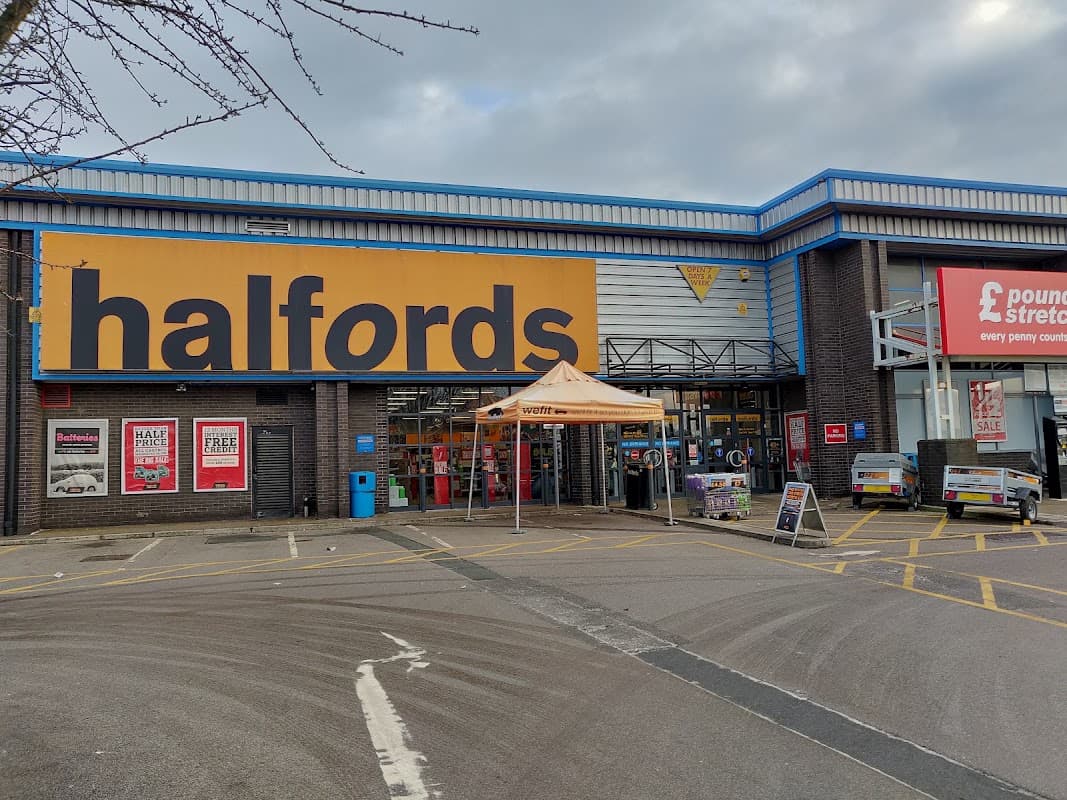 Halfords store entrance with large signage, orange canopy, and parking area in Dewsbury, Yorkshire.