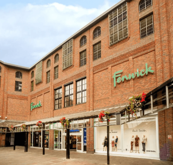 Brick building with large windows, "Fenwick" signage, and flower baskets adorning the entrance in Dewsbury, Yorkshire.