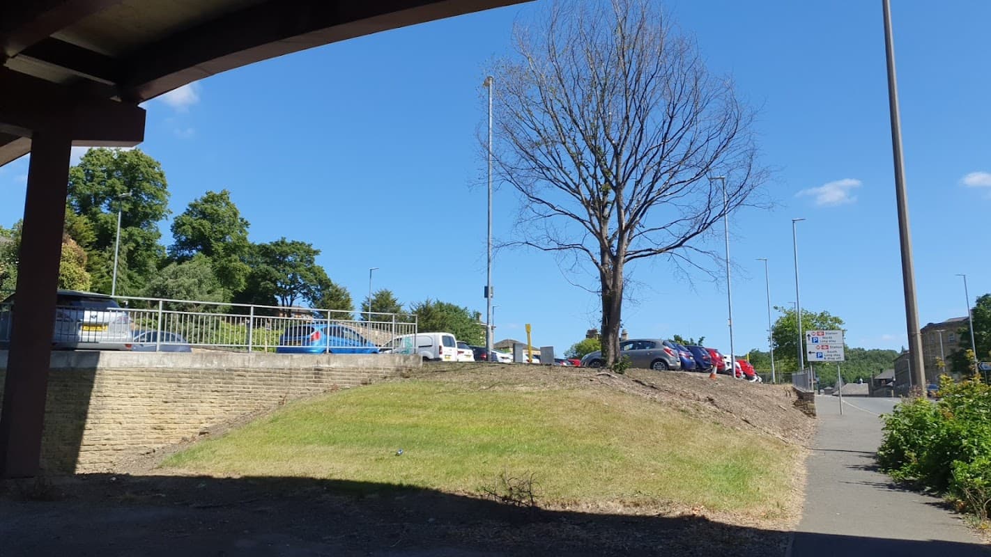 Railway station car park with parked cars, a tree, and signage under a clear blue sky in Dewsbury, Yorkshire.