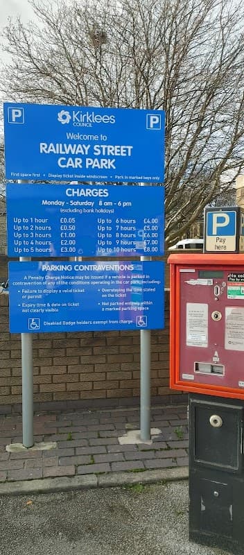 Blue sign detailing parking charges and regulations at Railway Street Car Park, Dewsbury, with a payment machine nearby.