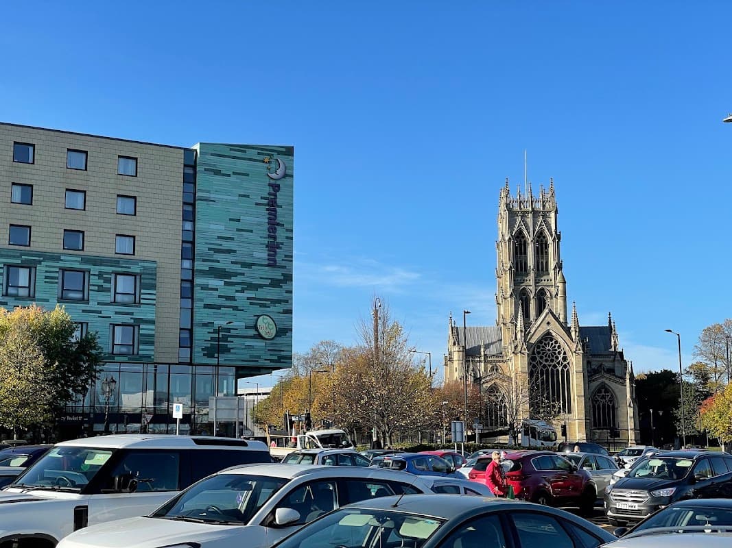 Pay & Display car park with cars, modern building, and a historic church under a clear blue sky in Doncaster.