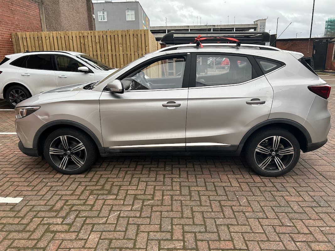 Silver SUV parked in a Pay & Display car park with brick paving and a wooden fence in the background.