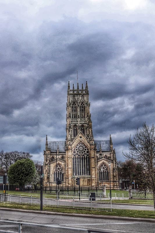 St. George's Church with intricate architecture under a dramatic cloudy sky, surrounded by greenery and a fence.
