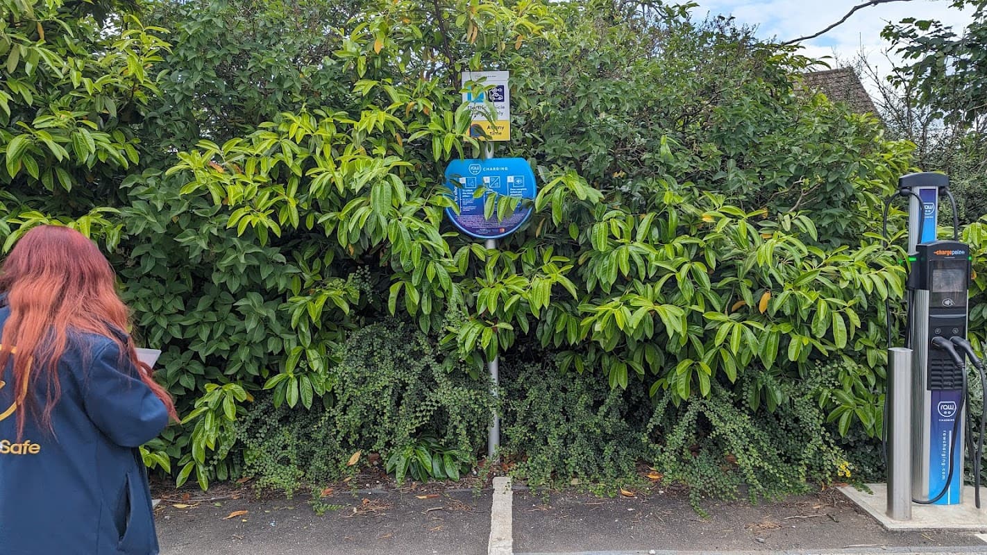 Pay & Display parking sign partially obscured by lush greenery, with a charging station visible nearby.