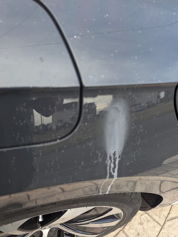 A close-up of a car's side, showing a streak of white substance against a dark surface.