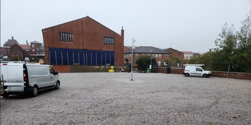 Gravel car park with two white vans, surrounded by brick buildings and a foggy sky in Driffield, Yorkshire.
