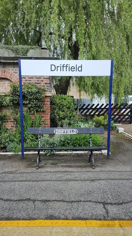 Driffield station sign with a bench, surrounded by greenery and a brick wall.