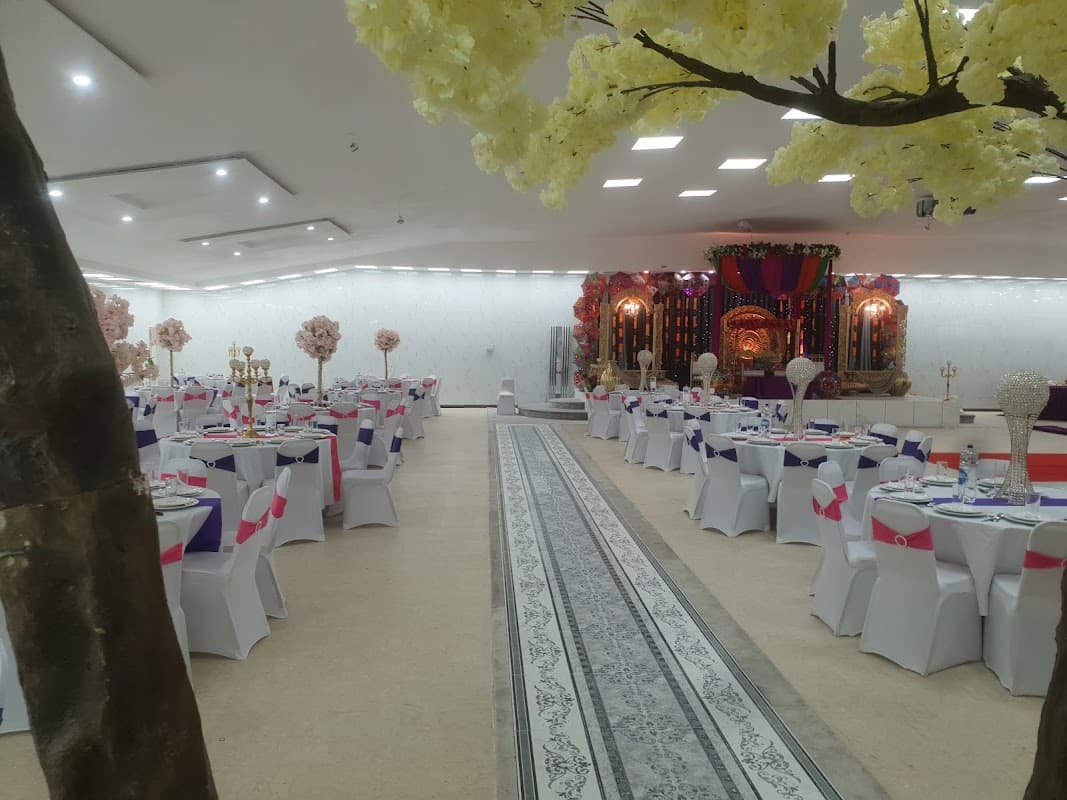Elegant banquet hall with white tables, colorful chair covers, floral decorations, and a stage backdrop.
