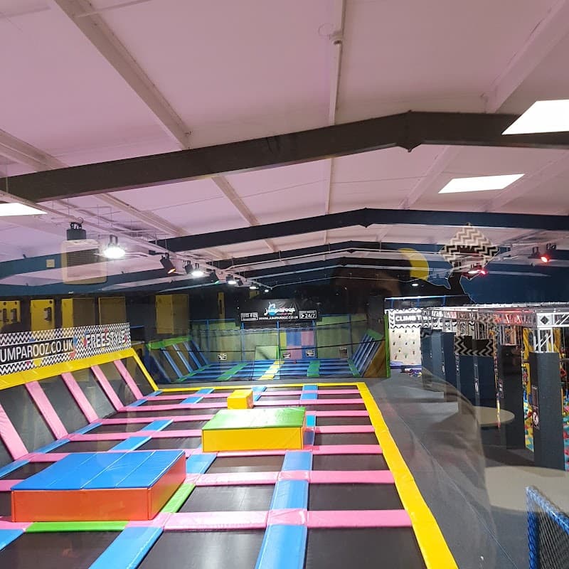 Colorful trampolines with various shapes and a climbing wall in a spacious indoor park.