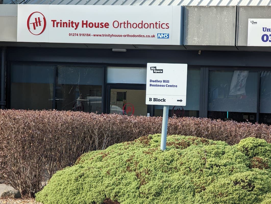 Sign for Trinity House Orthodontics with contact info, located in Dudley Hill Business Centre, surrounded by greenery.