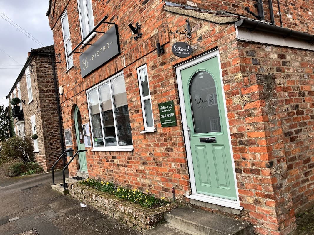 Brick building with a green door, signage for "Sixteen B" Bistro, and daffodils along the pathway in Dunnington, Yorkshire.
