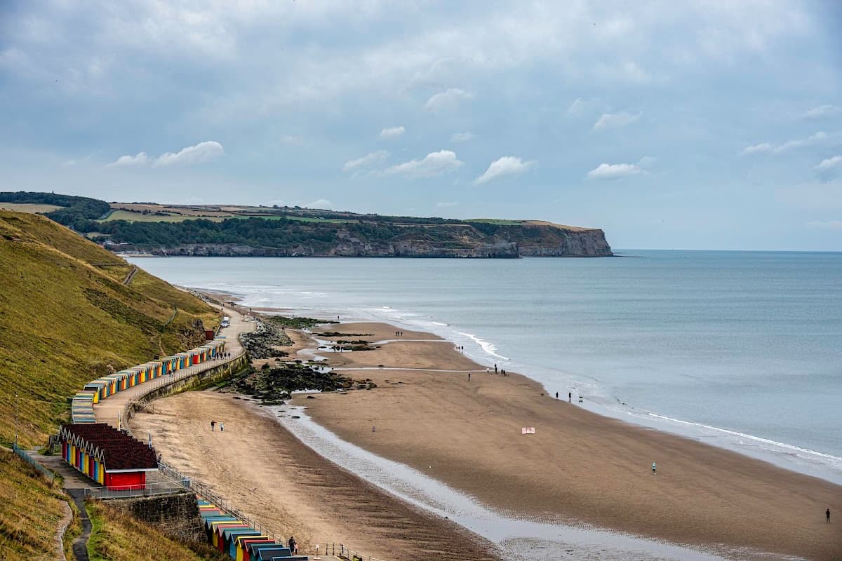 Colorful beach huts line the sandy shore, with gentle waves lapping at the beach and cliffs in the background.