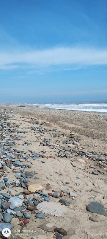 A sandy beach with scattered pebbles and gentle waves under a clear blue sky.