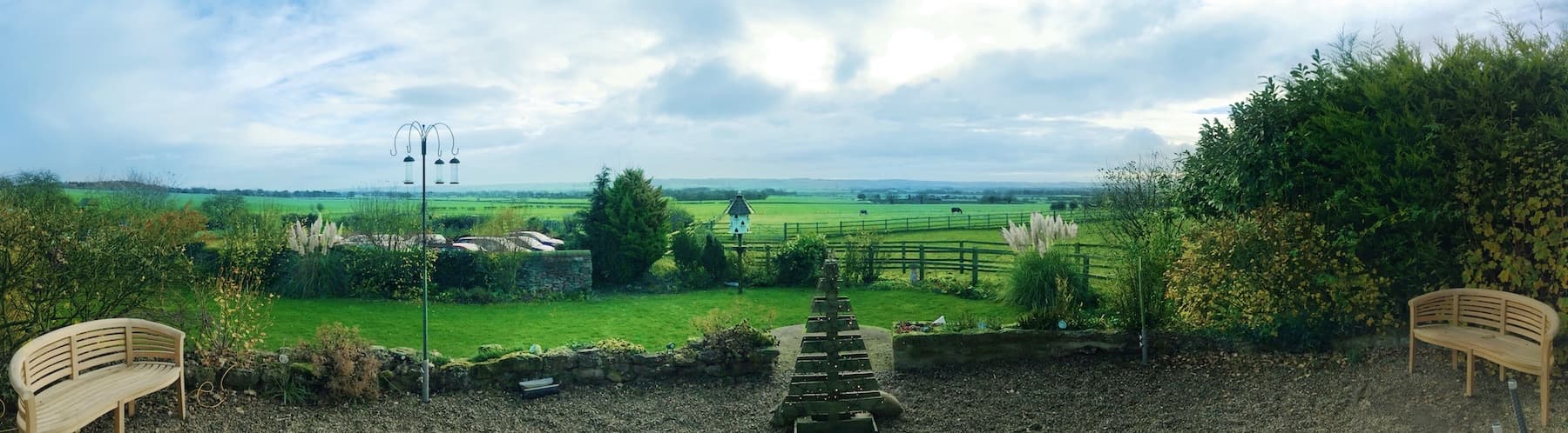 Panoramic view from Betton Farm showing green fields, benches, and a cloudy sky in East Ayton, Yorkshire.