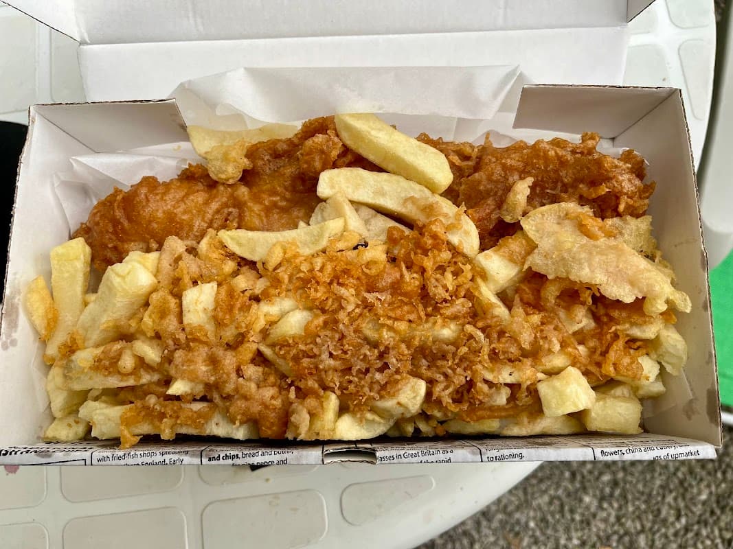 A takeaway box filled with golden-brown battered fish and crispy chips, resting on a white surface.