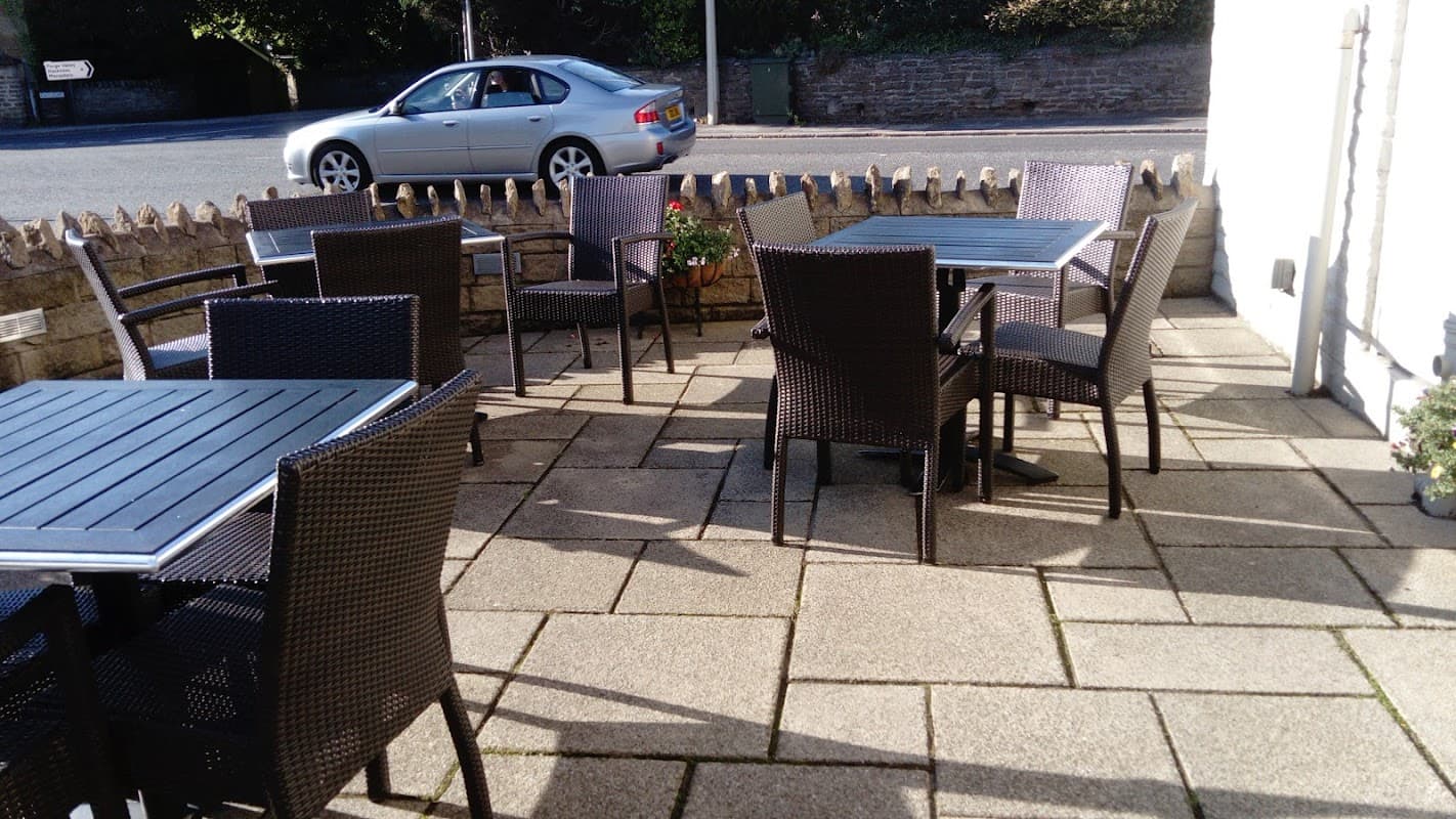Outdoor seating area with wicker tables and chairs on a paved patio, alongside a street with a parked silver car.