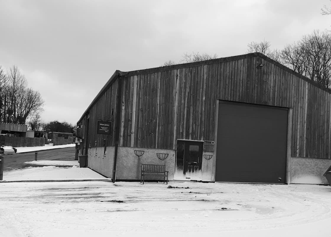 Wooden-clad workshop with a large garage door, snowy ground, and a bench outside in East Ayton, Yorkshire.