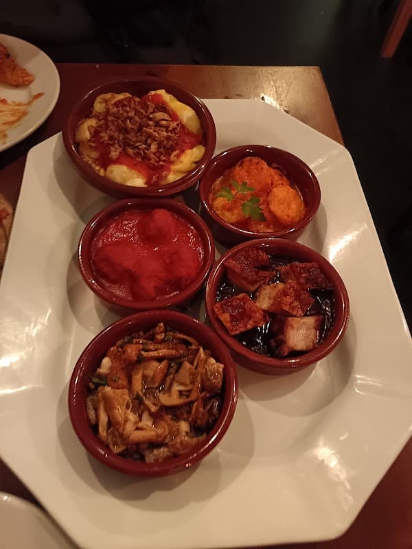 Five small bowls of colorful tapas dishes on a white platter, featuring various sauces and toppings.