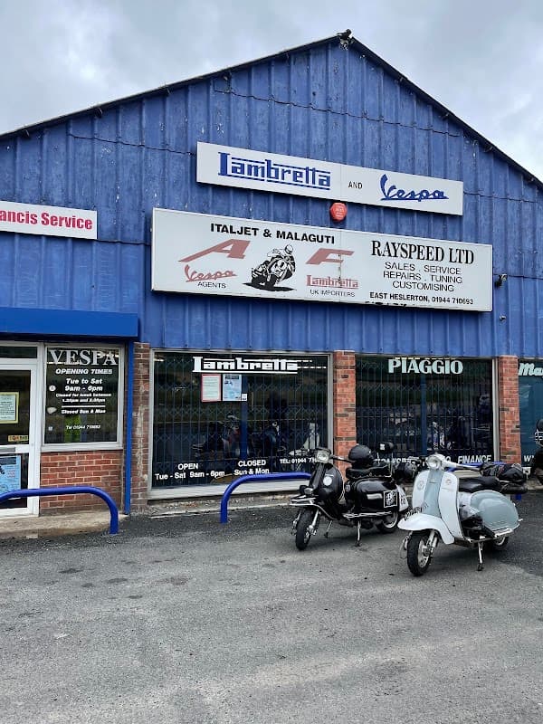 Blue shopfront with signs for Lambretta, Vespa, and Rayspeed Ltd; scooters displayed in the window.