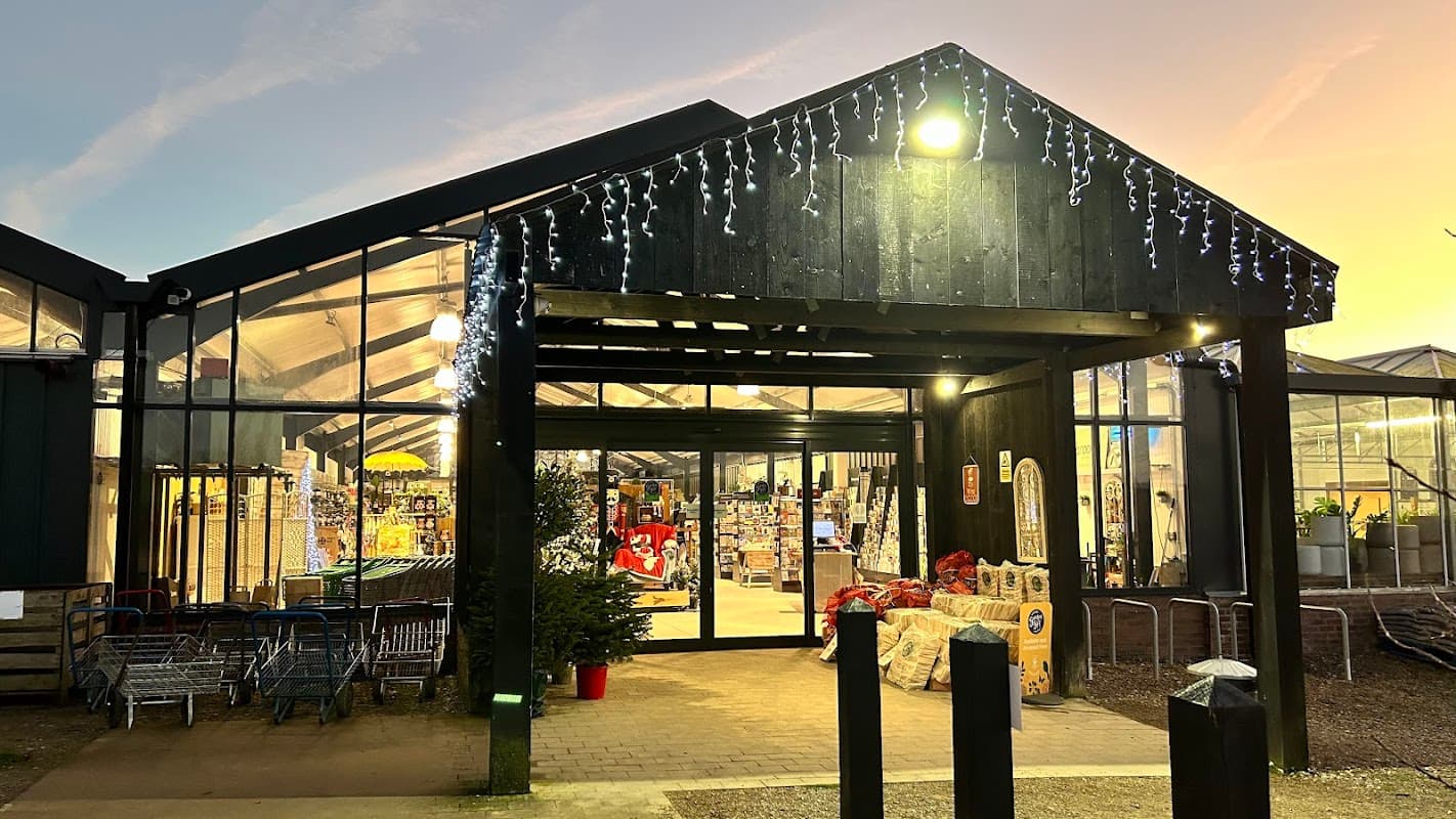 Entrance of Whitegates Nursery with festive lights, showcasing a glass structure and shopping carts outside.