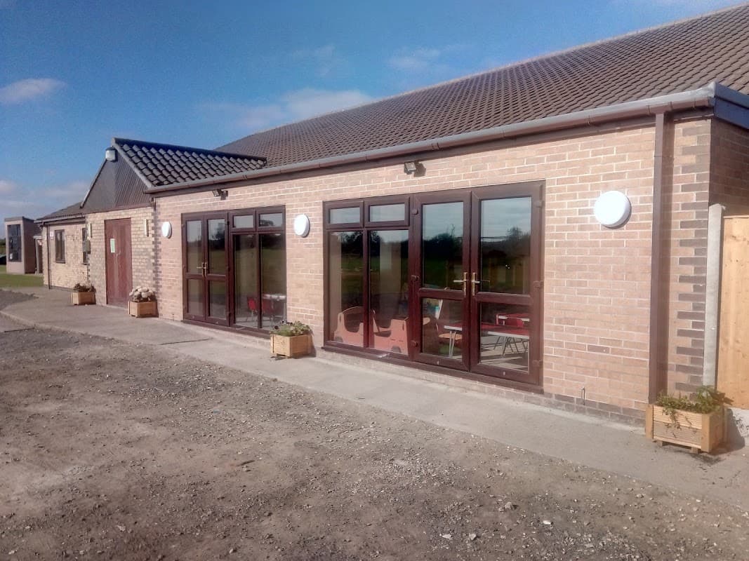 Eastrington Village Hall features large windows, a brick facade, and planters along the entrance against a clear blue sky.