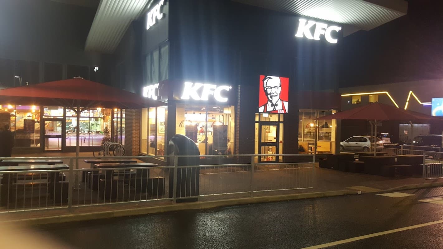 KFC location at night, featuring outdoor seating and a bright illuminated sign with Colonel Sanders' image.