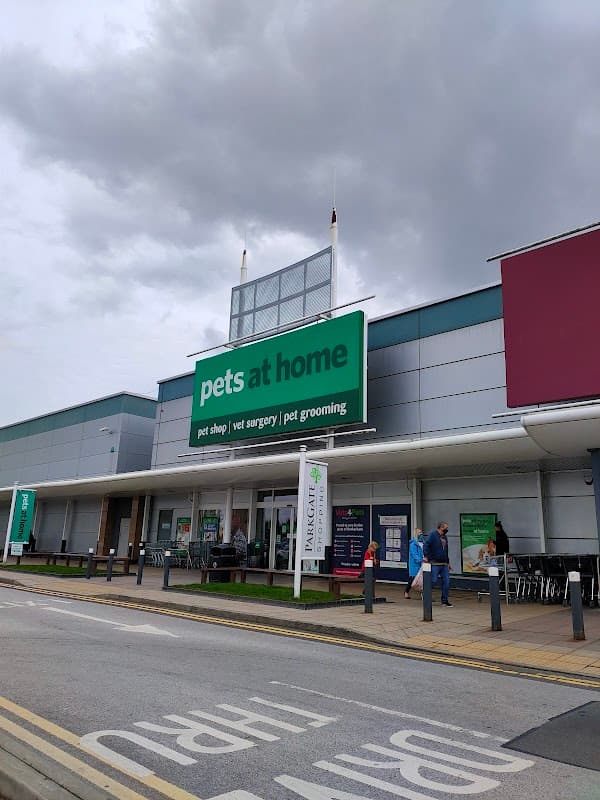Large green sign reading "pets at home" on a modern pet shop building, with shoppers and cloudy skies above.