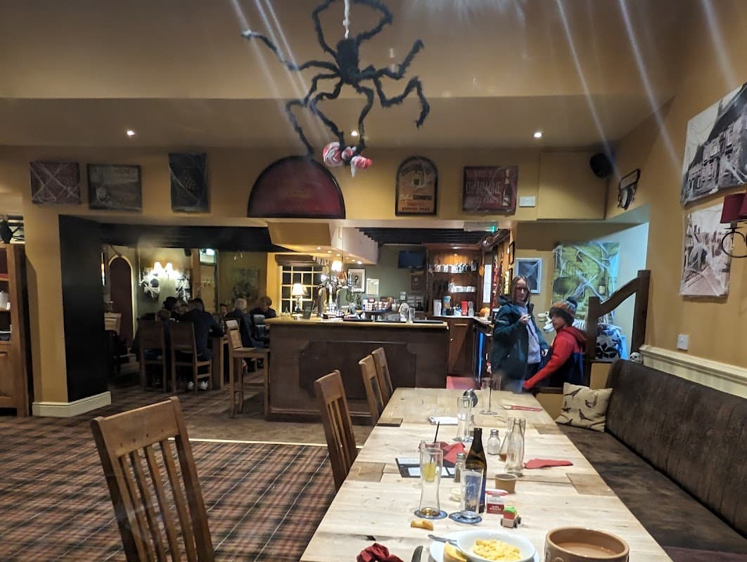 Interior of The Grapes Inn featuring wooden tables, a bar, patrons, and a spider decoration hanging from the ceiling.