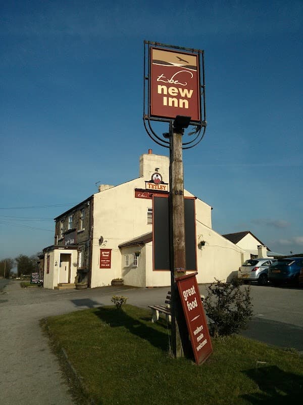 Sign for "The New Inn" bar with a white building and blue sky in Eccup, Yorkshire, featuring a grassy path.
