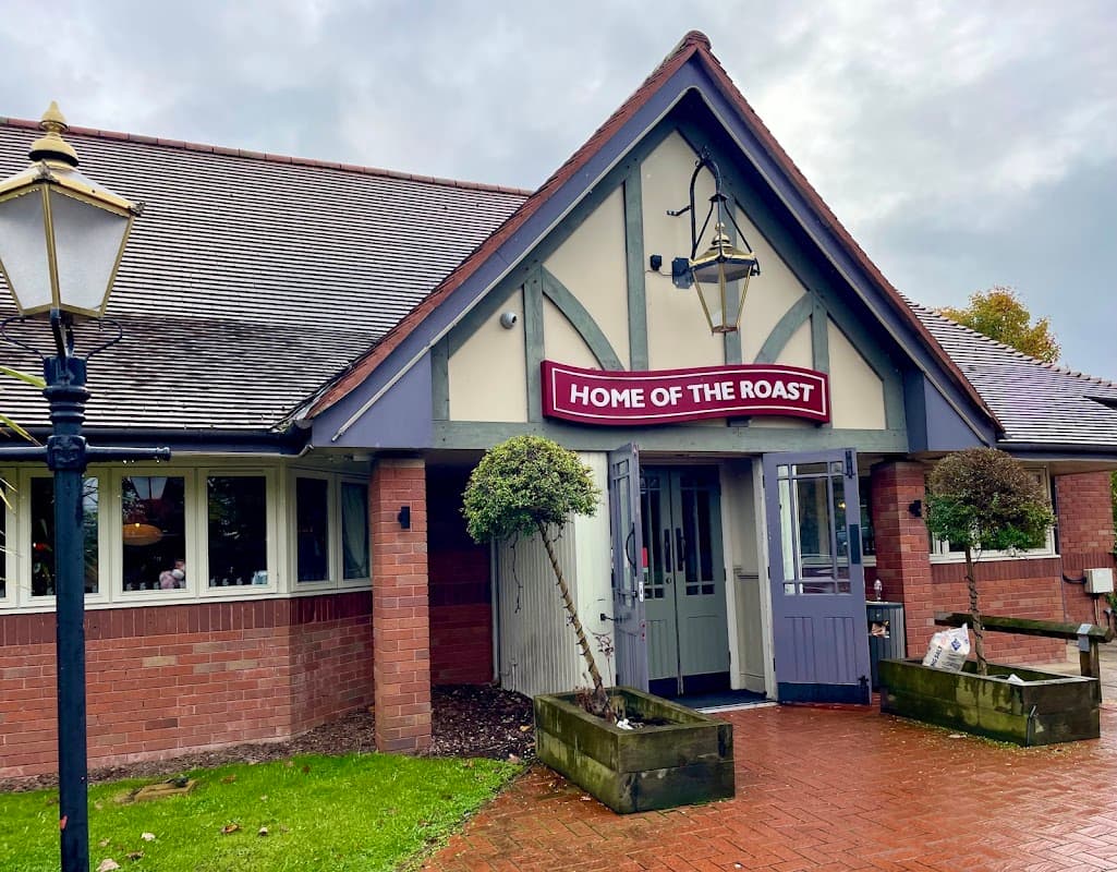 Quaint cafe entrance with "HOME OF THE ROAST" sign, lanterns, and landscaped greenery in Edenthorpe, Yorkshire.