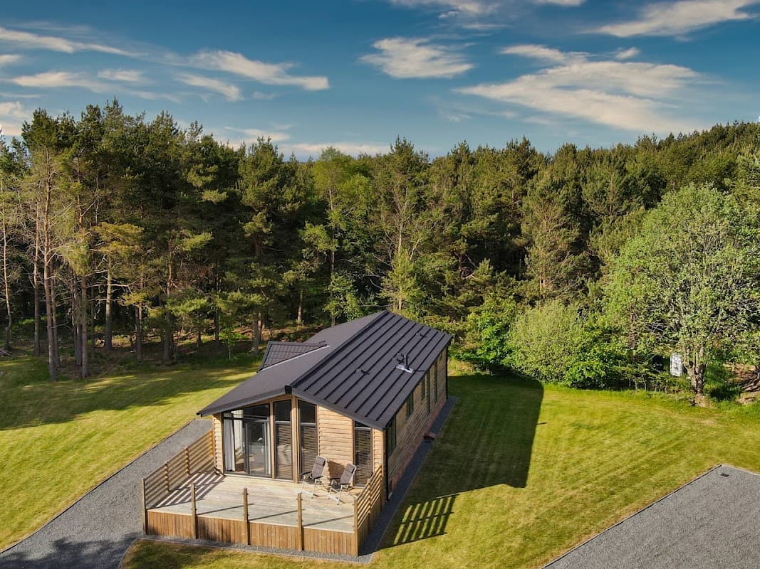 Modern wooden lodge with a deck, surrounded by lush greenery and trees at Ladycross Plantation Caravan Park in Egton.