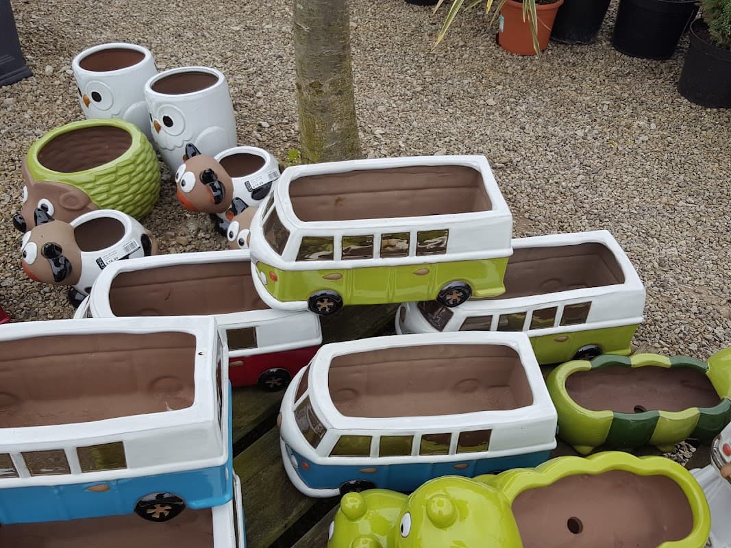 Colorful ceramic plant pots shaped like vintage vans and animals, displayed on gravel at The Green Frog Garden Shop.