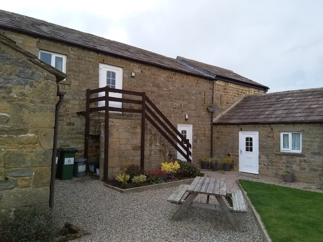 Stone cottages with a wooden staircase, picnic table, and garden in a rural setting.