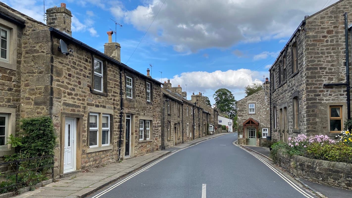 Stone buildings lining a quiet street, with a small entrance to a village institute and colorful flowers nearby.