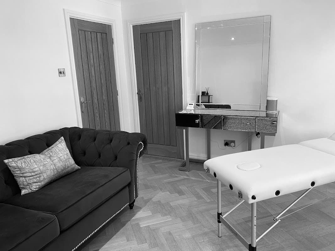 Chic treatment room with a black tufted sofa, mirrored table, and a massage bed on a wooden floor.
