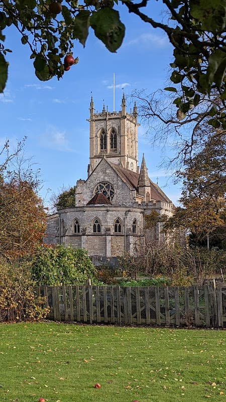 St Helen's Church features a tall tower, ornate stonework, and surrounded by trees and greenery under a blue sky.