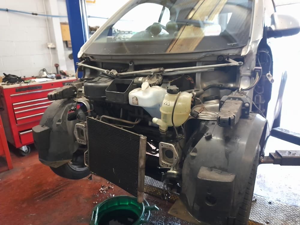 Car with exposed front components in a garage, tools and red tool chest visible in the background.